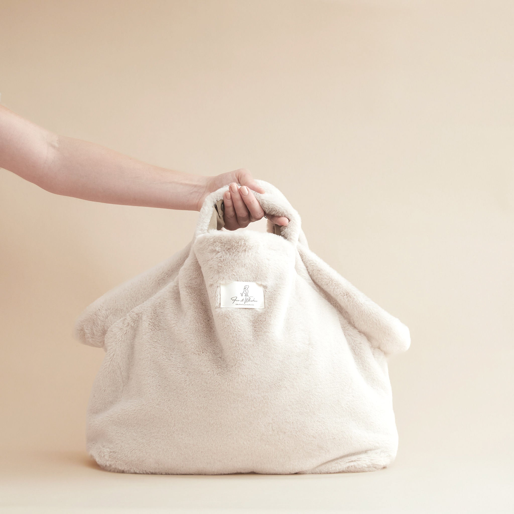 Beige fabric bag held by a hand on a beige background